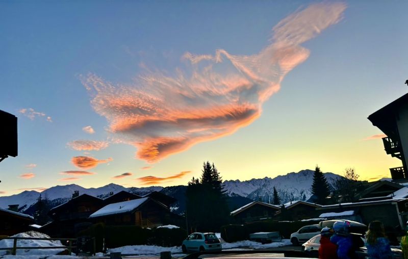 Pink clouds over snowy mountains and chalets at sunset