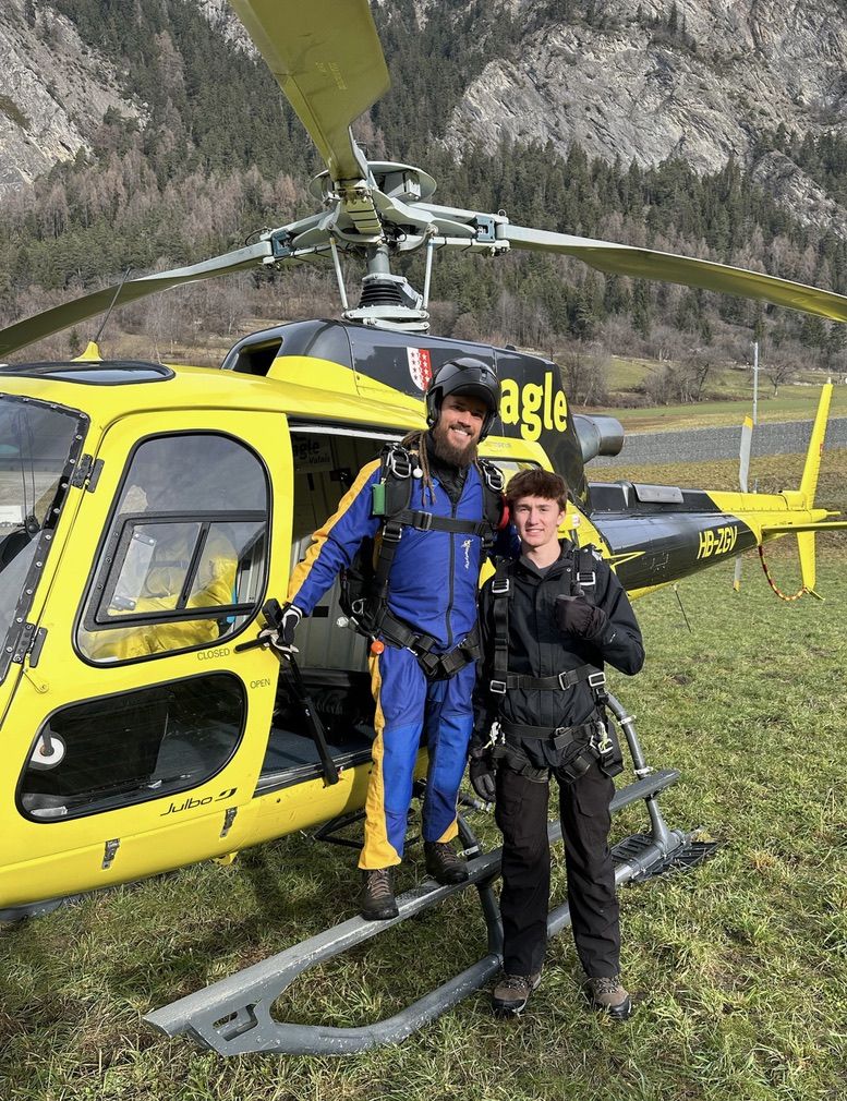 Max Gallinek in a harness next to a yellow helicopter in a Swiss valley